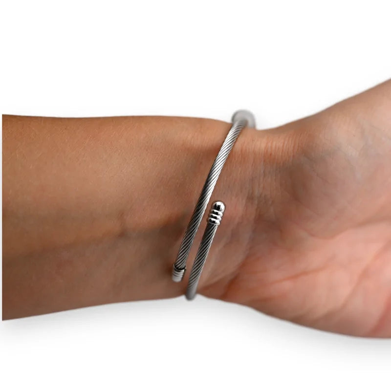 Bracelet rigide argenté en câble métallique avec fermoir ajustable porté sur un poi...